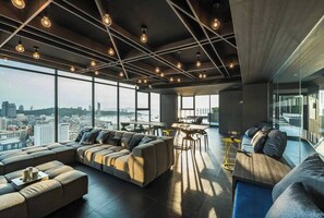 A spacious living area with a large sofa, a dining table, and a view of the cityscape through large windows. - Sea View 2 Bed Room Best of Location (Pattaya)
