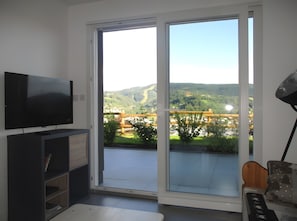 Una habitación con televisión sobre un mueble bajo, puerta corrediza de vidrio que da a un espacio exterior con vistas a un puente y colinas.