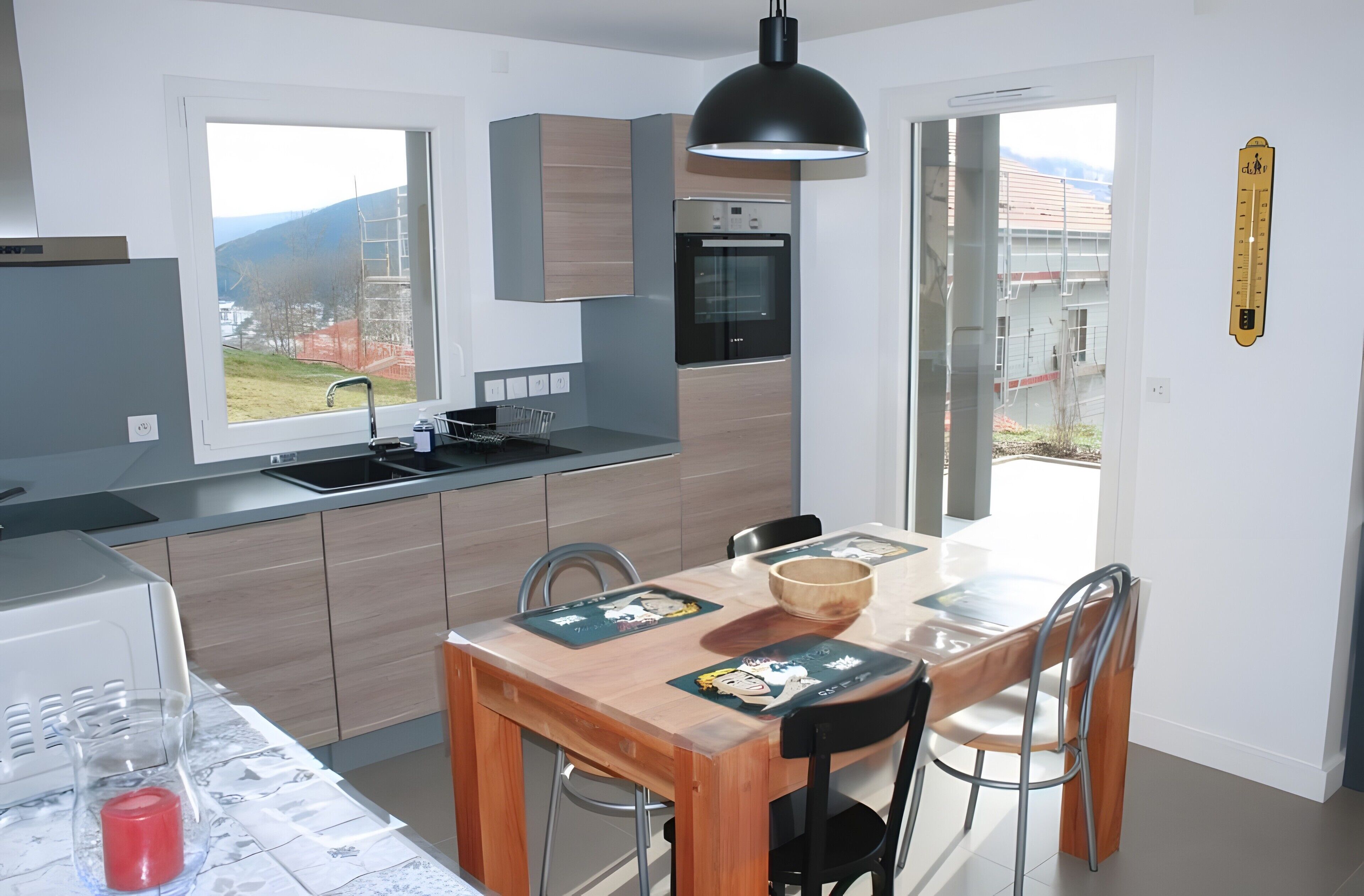 Una cocina moderna con horno integrado, una mesa de comedor con sillas y vistas al exterior.