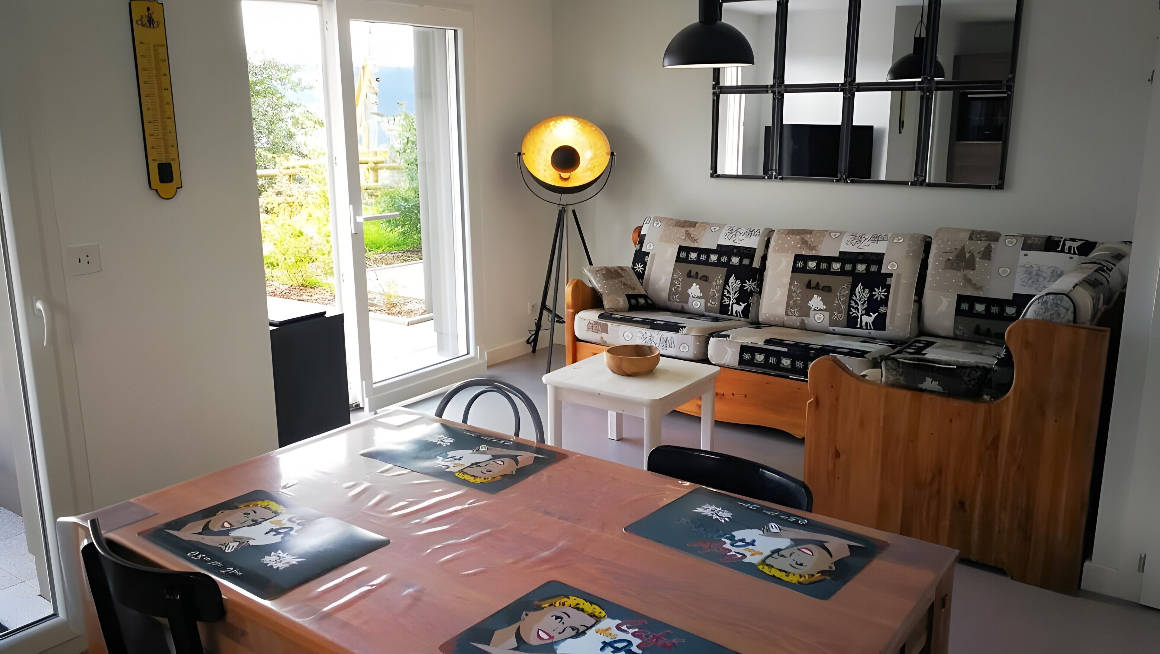 Een moderne woonkamer met een bank, een eettafel met placemats met stripfiguren, een vloerlamp en een groot raam.