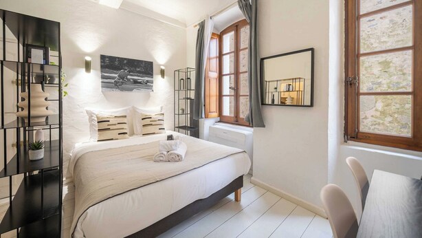 Een slaapkamer met een bed, nachtkastje, radiator, raam met gordijnen en een spiegel aan de muur.