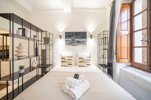 A modern hotel room with a large bed, two bedside tables, a black metal shelving unit, a window with curtains, and a wall-mounted picture. - Cozy Studio A/C 2P - Saint-Tropez (Saint-Tropez)