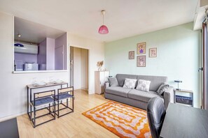 A living room with a grey sofa, a coffee table, a dining table with chairs, a pink pendant light, and a patterned rug. - Spacious Studio 2P - Near La Défense (Courbevoie)