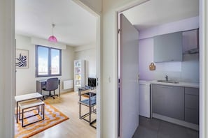A modern apartment with a kitchenette, a desk with a chair, a bookshelf, and a window with a view. - Spacious Studio 2P - Near La Défense (Courbevoie)