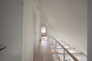 A narrow hallway with a wooden floor leading to a staircase with a glass railing. - New-build with sea views on Samsø (Samsø)