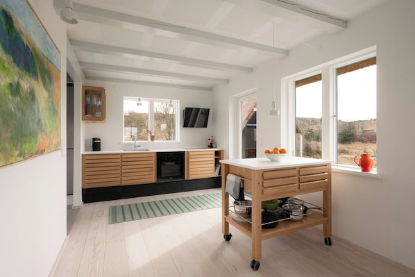 A modern kitchen with wooden cabinets, a built-in oven, and a window with a view of the countryside. - New-build with sea views on Samsø (Samsø)