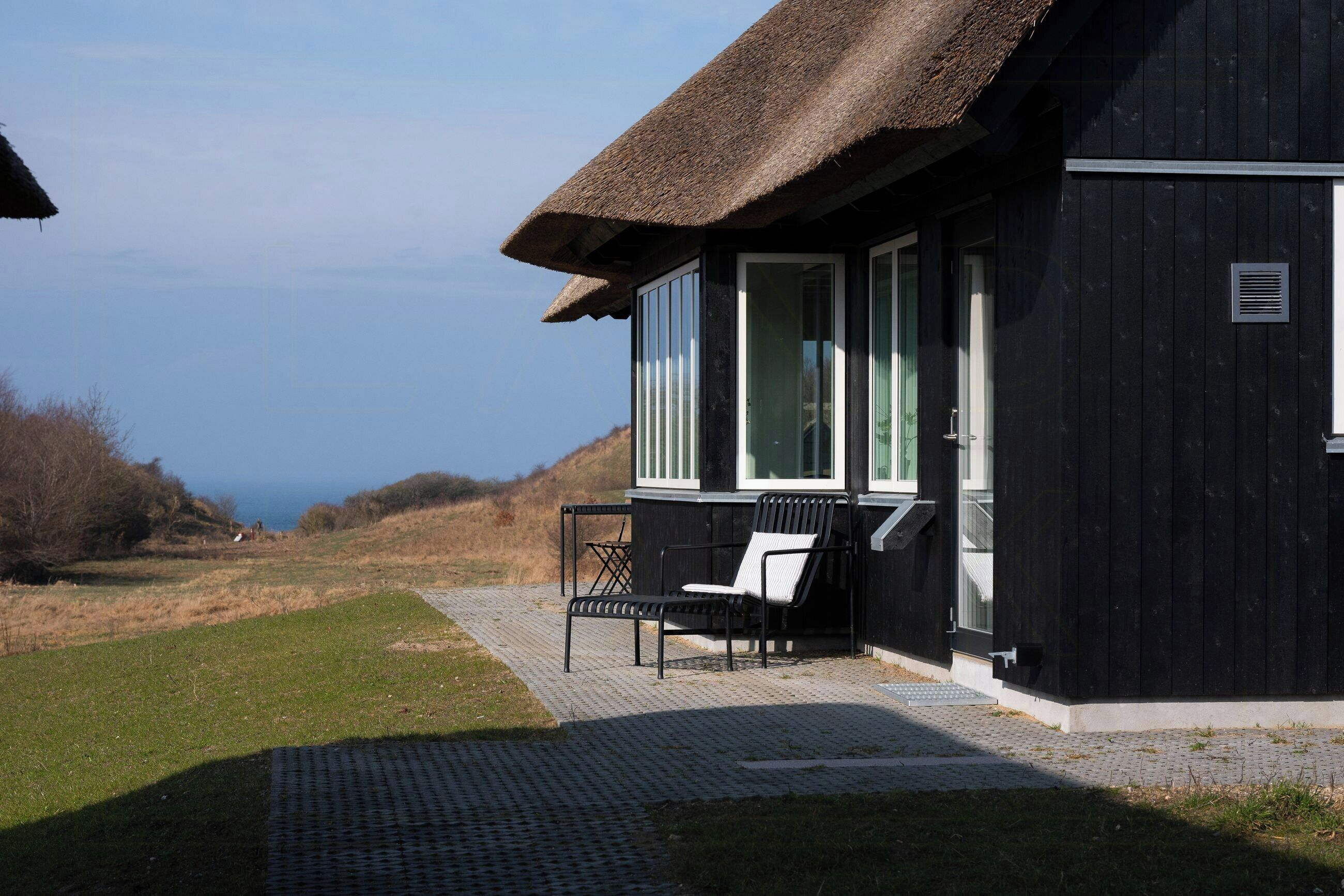 A black building with a thatched roof, a bench, and a view of the sea.