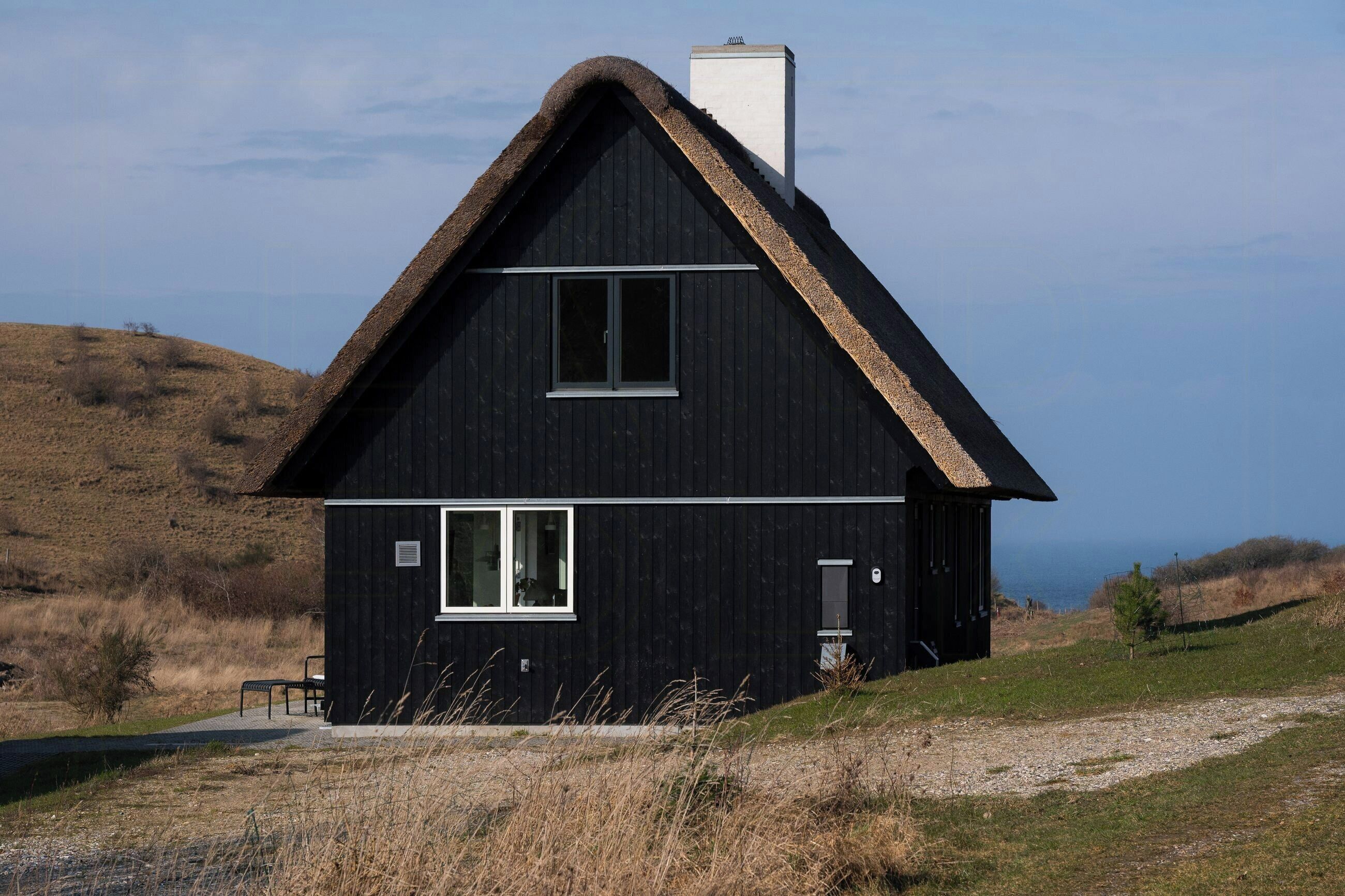 Een zwart houten huis met rieten dak, schoorsteen en raam.