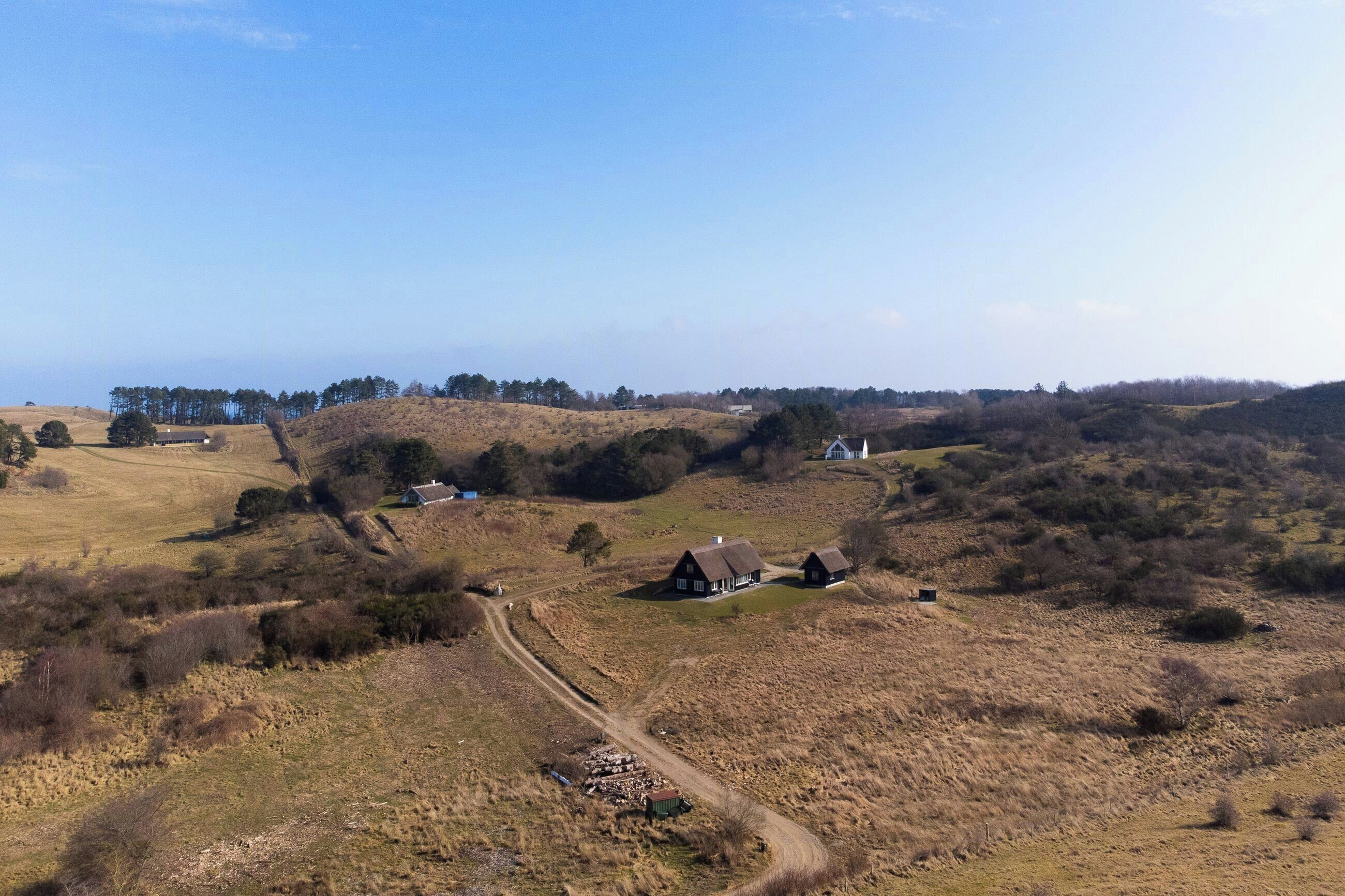 Un paysage rural caractérisé par des collines douces, un chemin de terre et plusieurs maisons traditionnelles.