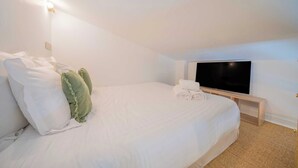 Habitación de hotel con cama, almohadas, televisión de pantalla plana y mesita de noche.