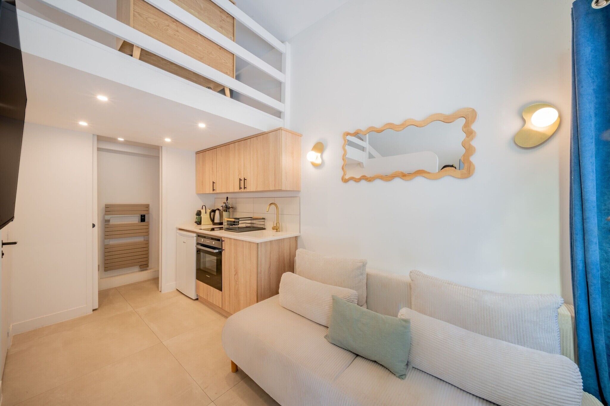 A modern apartment with a loft bedroom, a kitchenette, and a living area with a sofa.