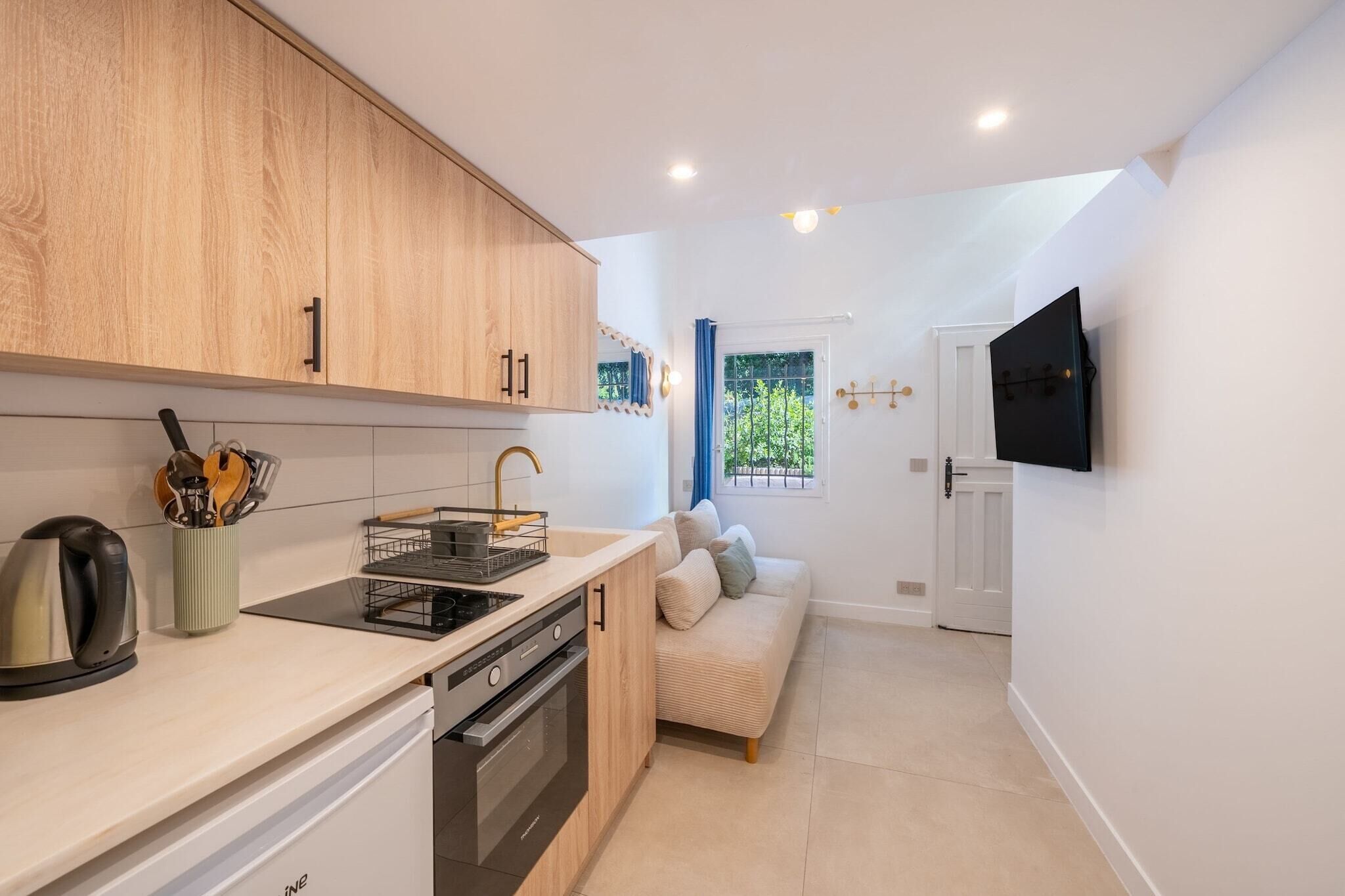 A compact kitchen with modern appliances, a dining area with a sofa, and a TV mounted on the wall.