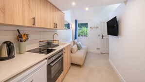 Una cocina compacta con electrodomésticos modernos, un área de comedor con sofá y un televisor montado en la pared.