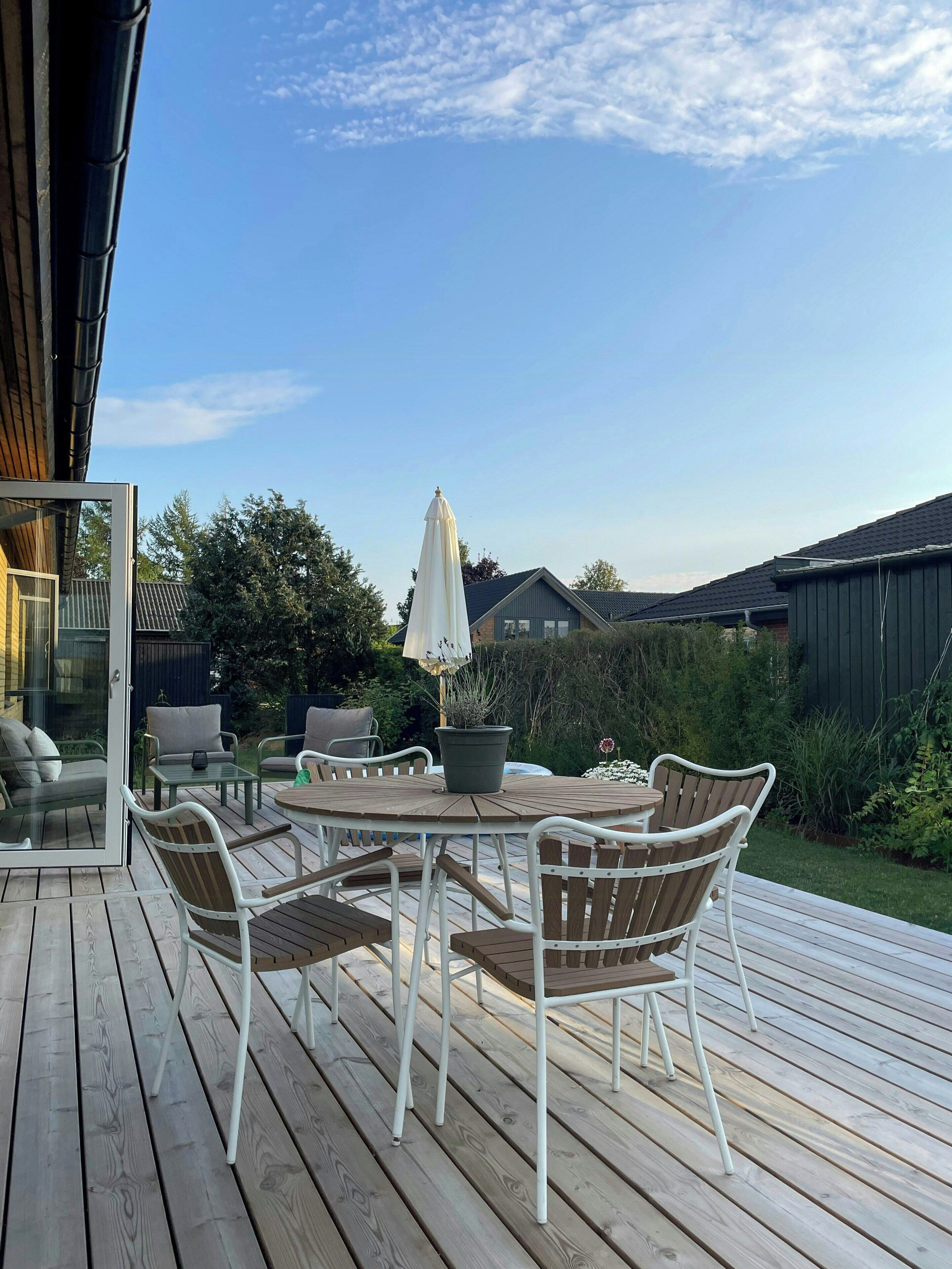 An outdoor deck with a round table and chairs, a potted plant, and a white umbrella.