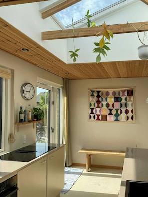 A modern kitchen with a skylight, wooden ceiling beams, a clock, and a colorful geometric wall art piece. - Retro 70s house with lake views in Jelling (Jelling)