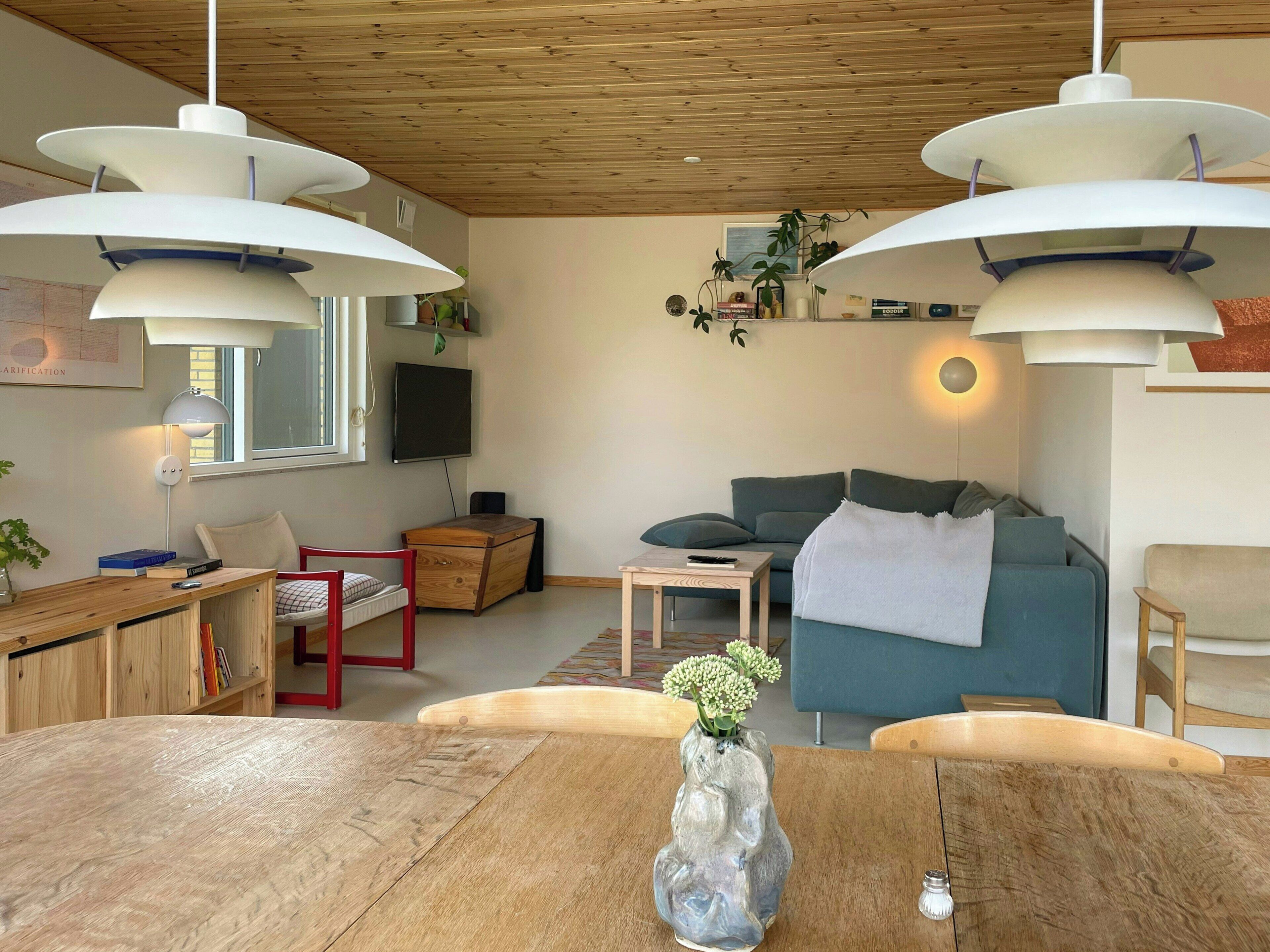 A modern living room with a wooden ceiling, a blue sofa, a wooden dining table, and pendant lighting.