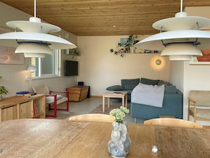 A modern living room with a wooden ceiling, a blue sofa, a wooden dining table, and pendant lighting.