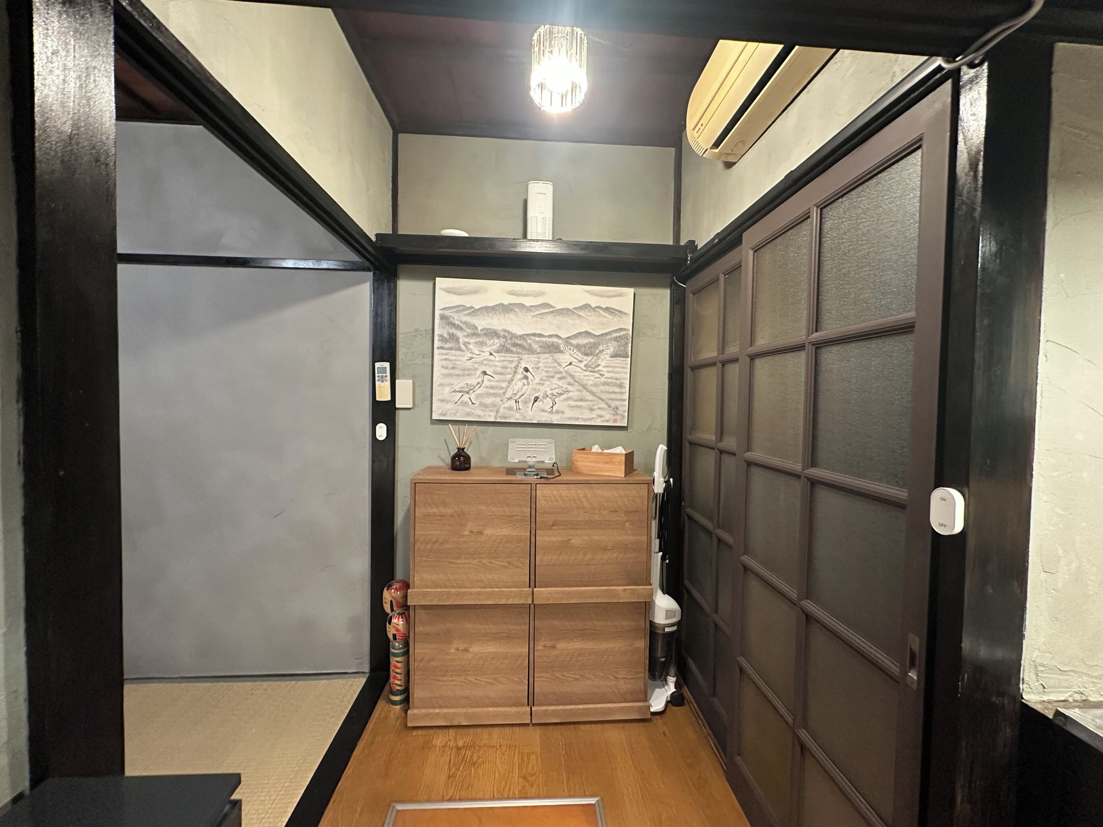 A traditional Japanese interior with a wooden cabinet, a painting, and a sliding door.