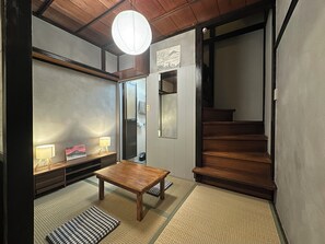 A traditional Japanese room with tatami flooring, a wooden table, a sofa, a hanging light fixture, and a staircase. - Rocket House, Traditional Japanese Home in Tokyo (Shinagawa City)
