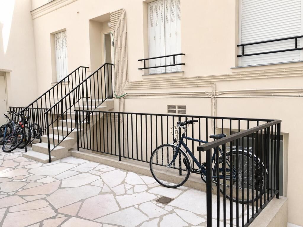 A building with a stone-paved courtyard, a staircase with black railings, and bicycles parked outside.