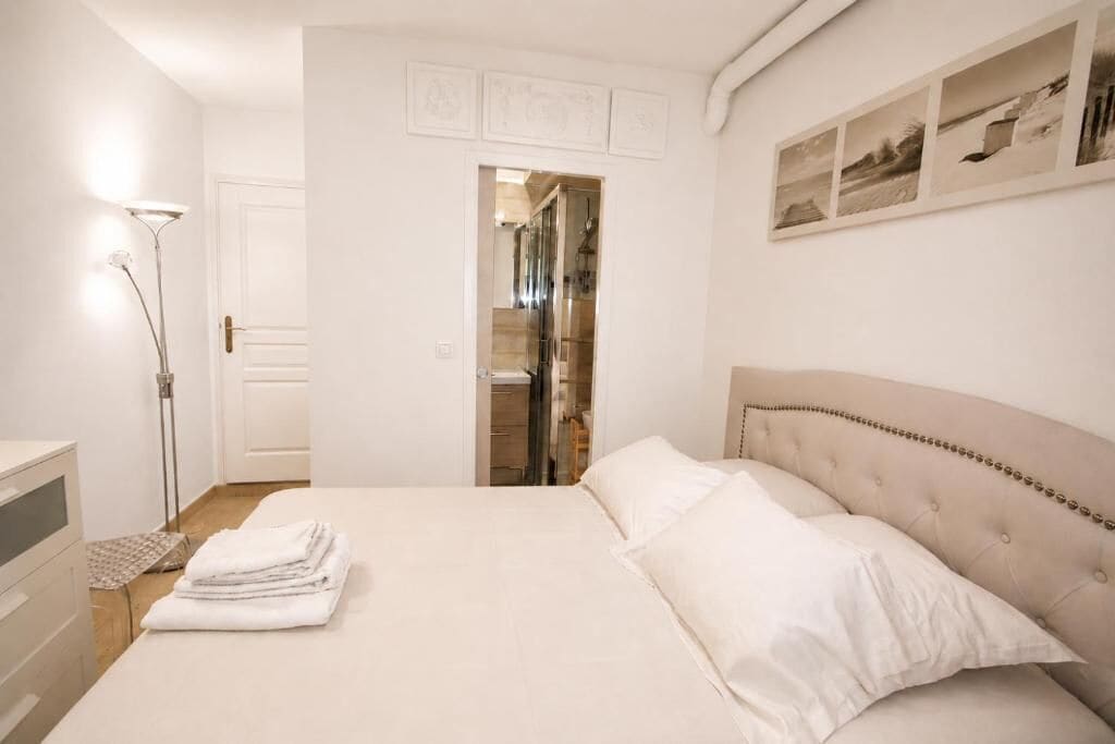 A hotel room with a bed, a bedside lamp, a door, and a wall with framed pictures.
