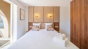 Une chambre d’hôtel avec un grand lit, deux tables de chevet, une tête de lit en bois et une vue sur l’extérieur à travers une porte vitrée.
