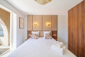 Una habitació d'hotel amb un llit gran, dues taules de nit, un panell de fusta al capçal i una vista per una porta de vidre.