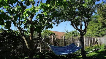 Una hamaca entre árboles en un patio trasero con una valla de madera y una casa al fondo.