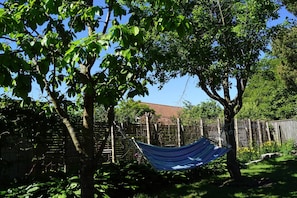 A hammock between trees in a backyard with a wooden fence and a house in the background.
