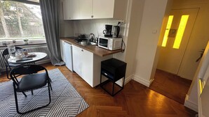 Ett kompakt kök med mikrovågsugn, kaffebryggare och en liten matplats med bord och stolar.