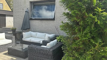 Un área de estar al aire libre con un sofá y sillones de mimbre, una mesa y una planta en maceta.