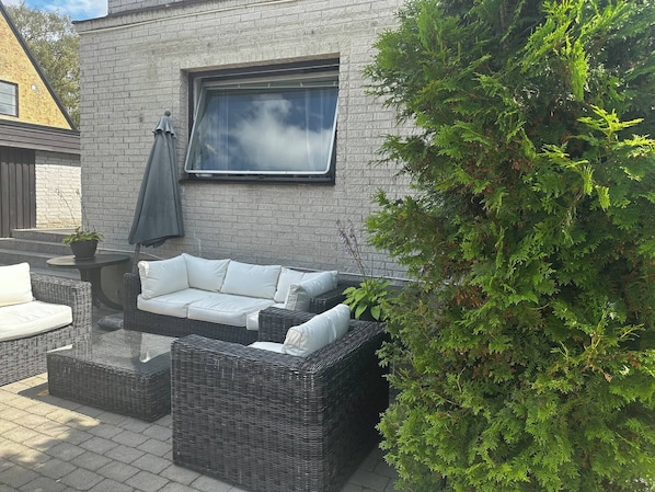 An outdoor seating area with a wicker sofa and chairs, a table, and a potted plant.