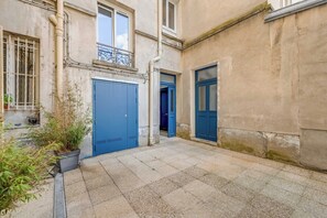 A courtyard with two blue doors, a concrete floor, and a building with a balcony. - Design Studio for 2P – Batignolles (Paris)
