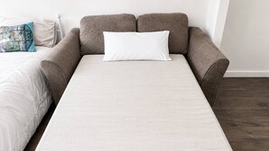 A single bed with a white sheet and a grey blanket, a grey sofa with a white pillow, and a patterned throw pillow. - Spacious 2BR Sleeps 7,  Long Stays (Greater London)