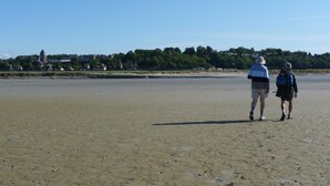 Two people walking on a sandy beach with a clear sky, a distant building, and trees. - Pretty little Picardy house by the water (Epagne-Epagnette)