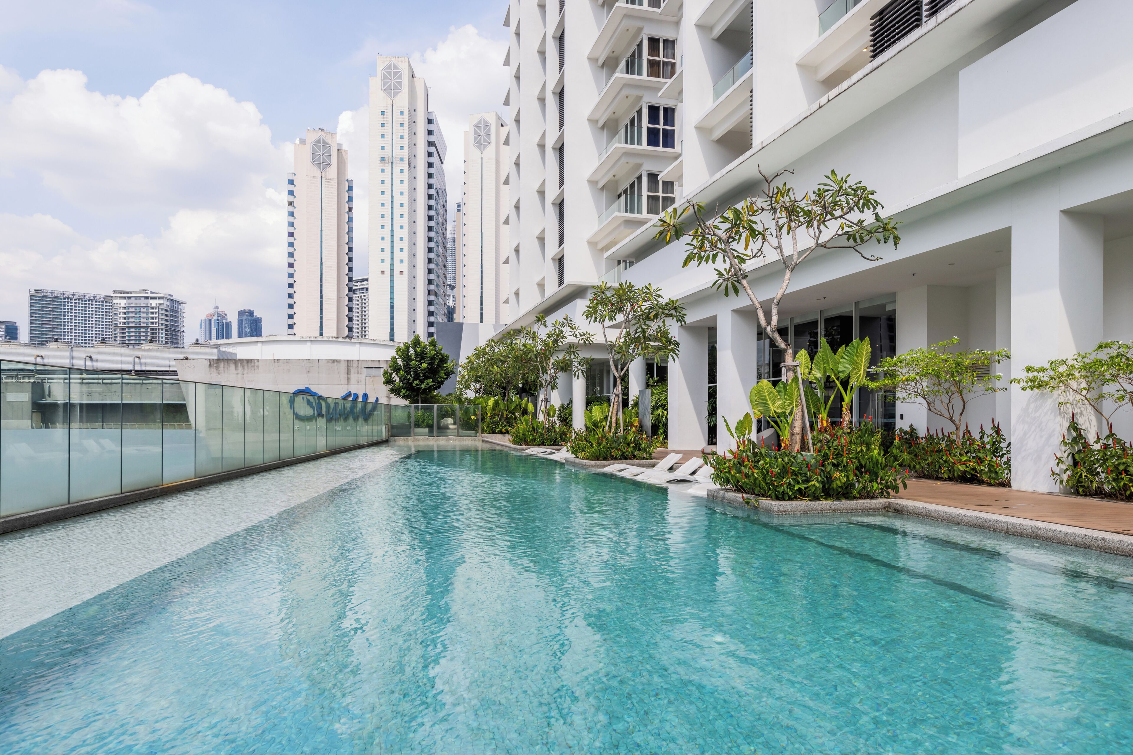 Un hotel moderno con piscina infinita en la azotea, rodeado de exuberante vegetación y vistas a un paisaje urbano.