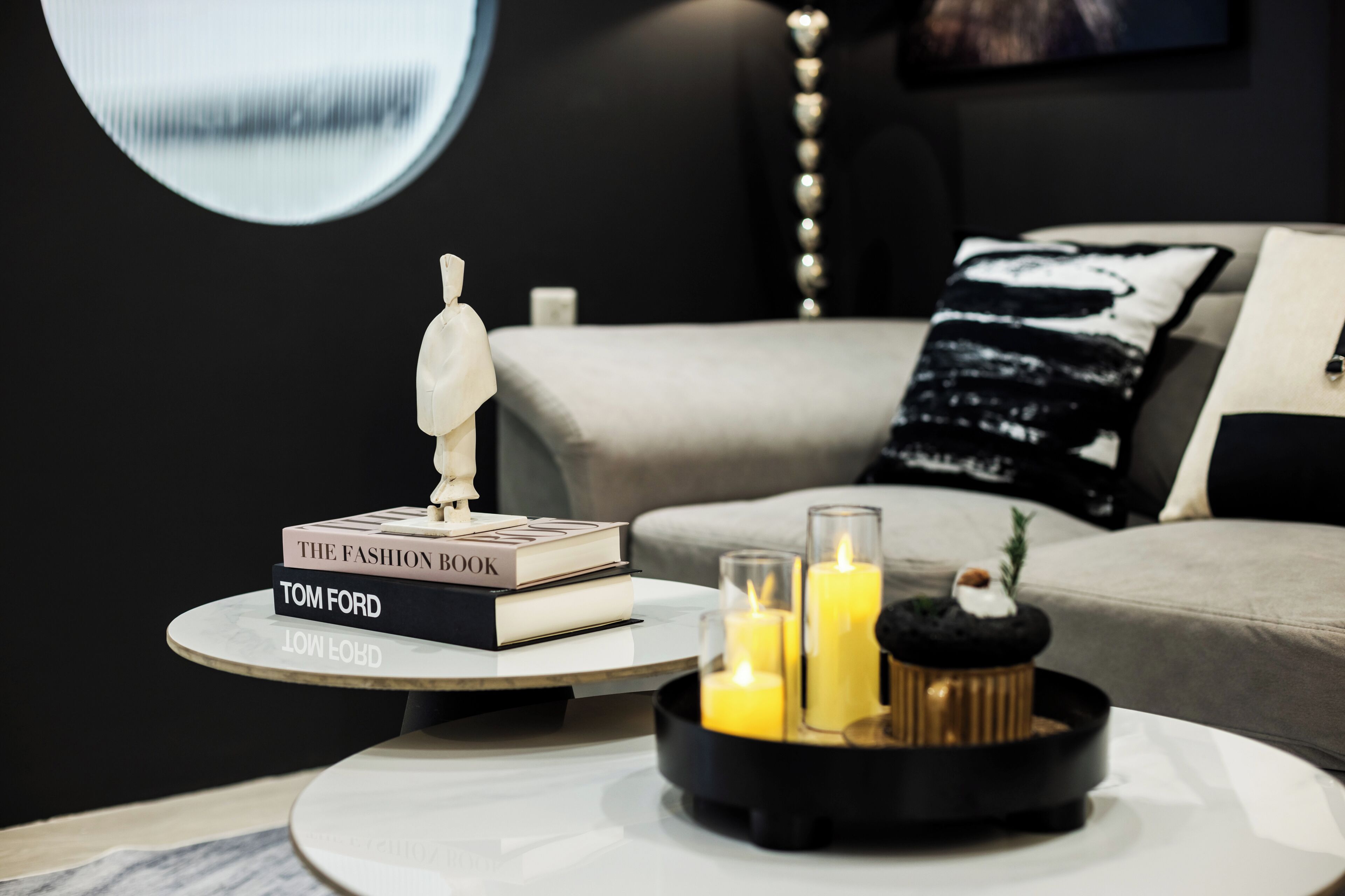A modern living room with a round coffee table, a stack of books, a decorative sculpture, and candles.