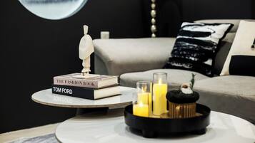 A modern living room with a round coffee table, a stack of books, a decorative sculpture, and candles.