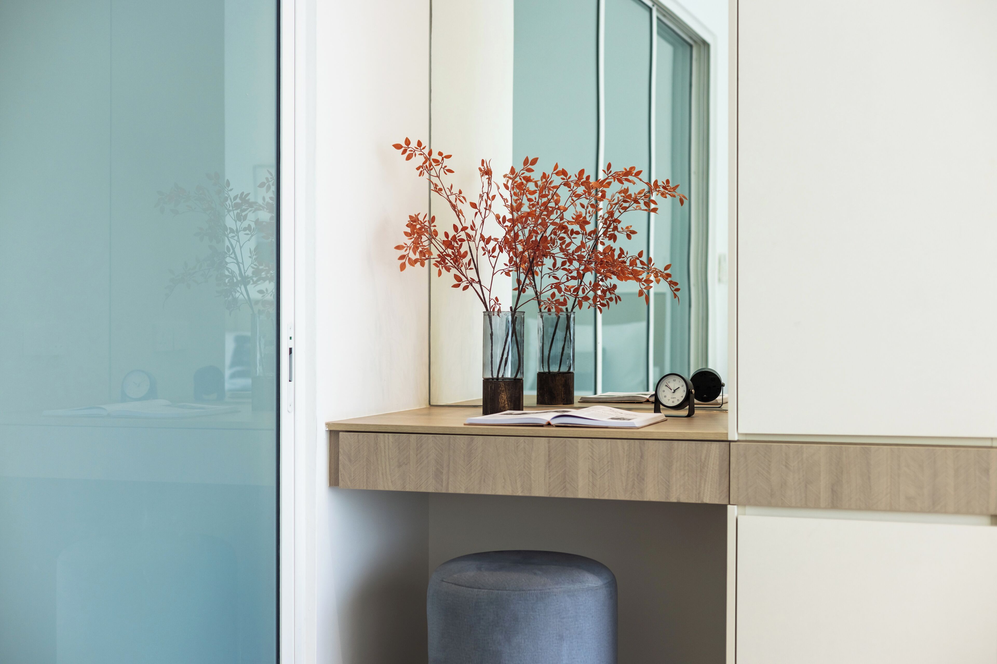 A modern room with a wooden desk, a window, and a vase with red leaves.
