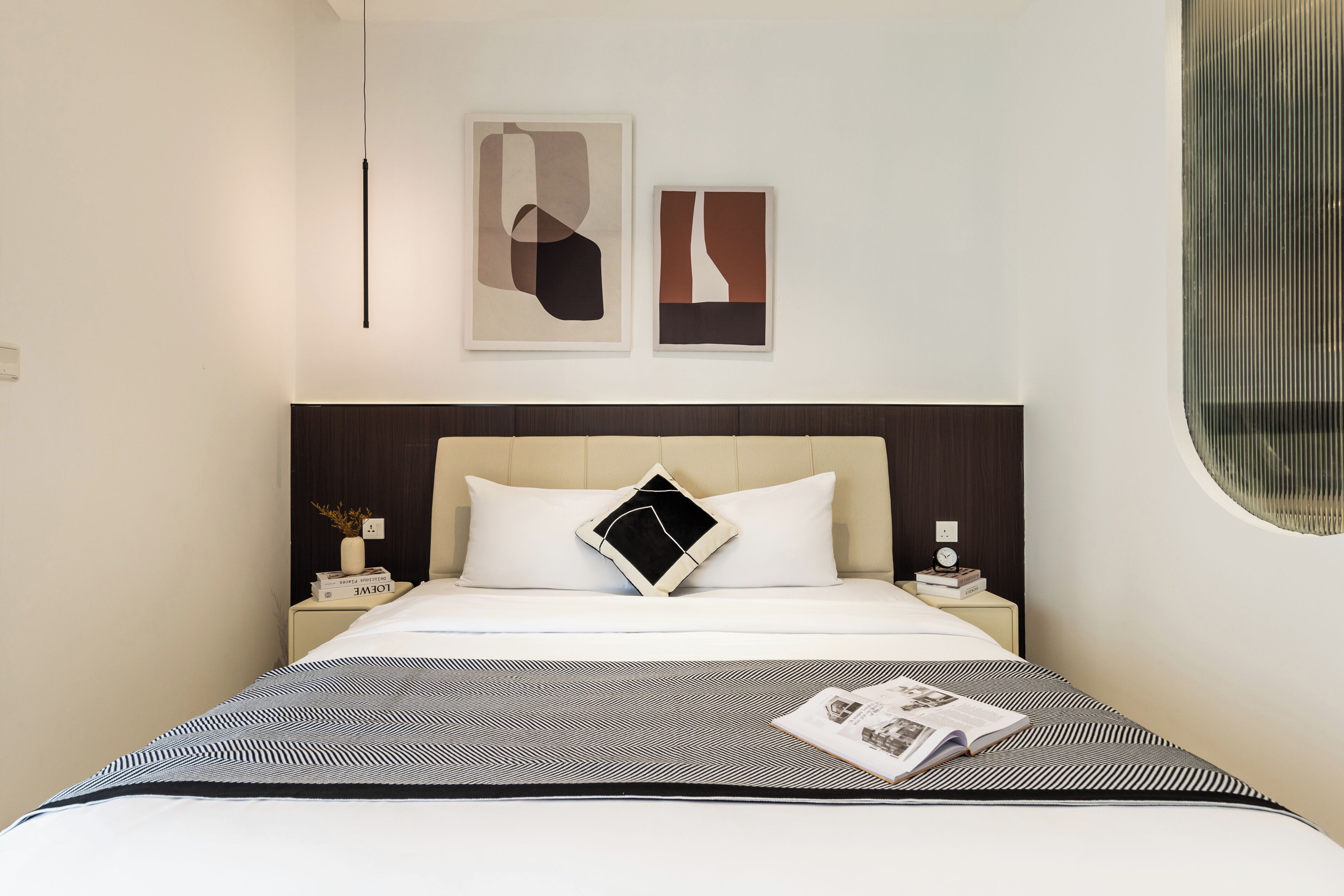 A modern hotel room with a large bed, a nightstand, a wall-mounted light, and abstract artwork.
