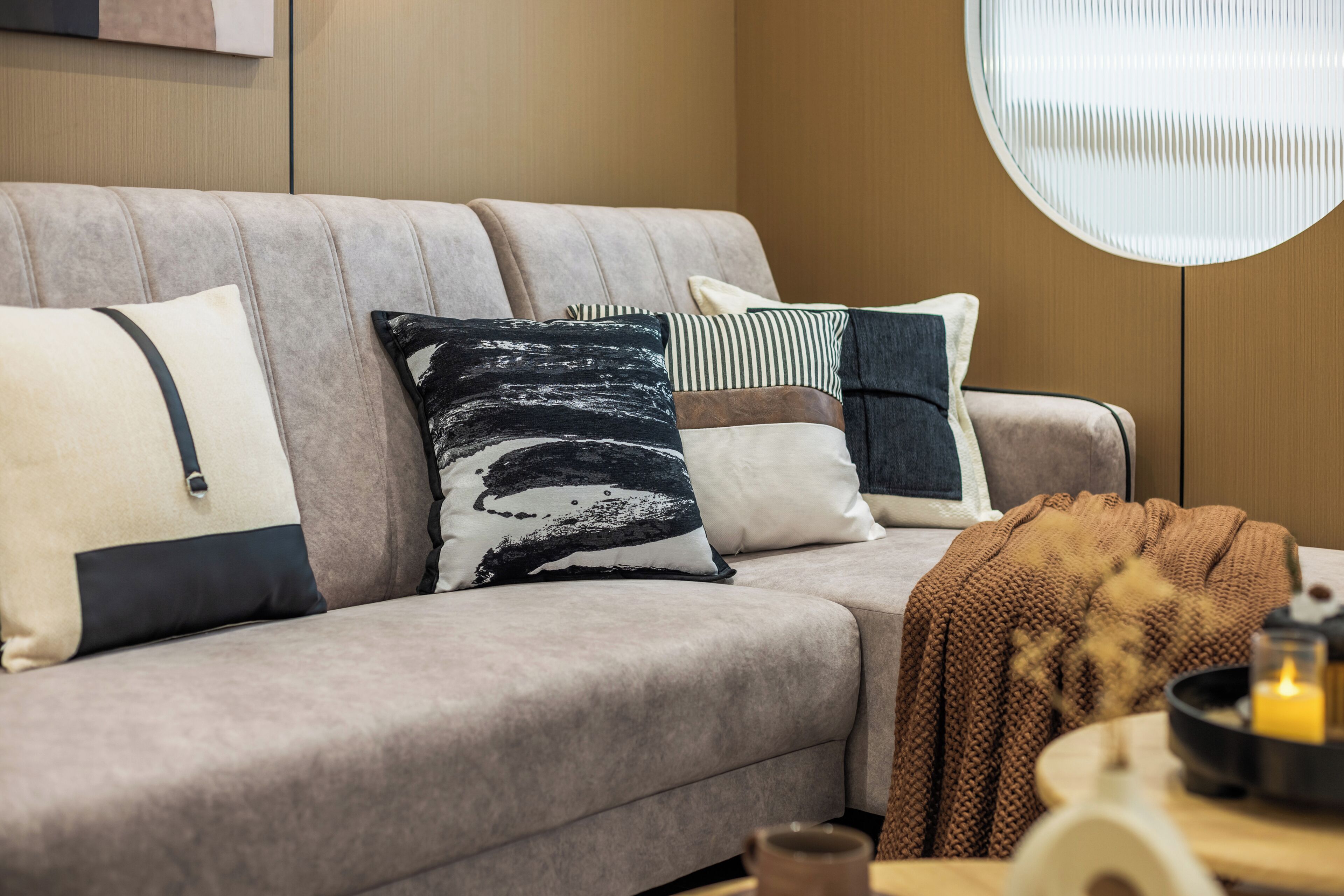 Una sala de estar moderna con un sofá, almohadas, un plaid de punto, una vela y una mesa redonda con una vela.