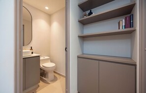 A modern bathroom with a toilet, a sink, and a mirror. There are shelves above the toilet with books and decorative items. - Live in Provenza Modern 1 BR   security (Medellín)