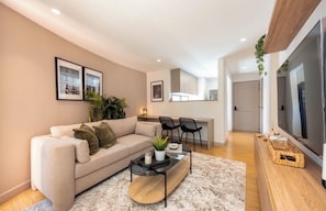A modern living room with a sofa, coffee table, and chairs. There is a television and a kitchen area in the background. - Live in Provenza Modern 1 BR   security (Medellín)