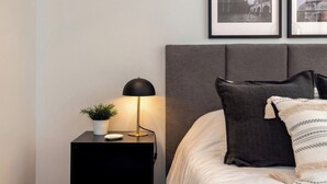 A neatly made bed with a grey headboard, a bedside table with a lamp, and two framed pictures on the wall. - Live in Provenza Modern 1 BR   security (Medellín)