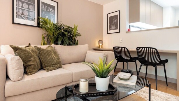 A living room with a sofa, a coffee table, and two chairs. There are framed pictures on the wall and a plant on the sofa. - Live in Provenza Modern 1 BR   security (Medellín)