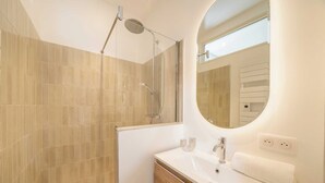 Ein modernes Badezimmer mit einer gläsernen Duschkabine, einem weißen Waschtisch mit Spiegel und beige gefliesten Wänden.