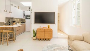 A modern living space with a kitchen, dining area, and a large flat-screen TV mounted on the wall.