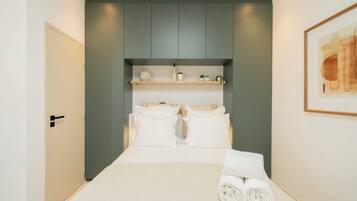 A hotel room with a bed, a wardrobe, a shelf with toiletries, and a framed picture on the wall.