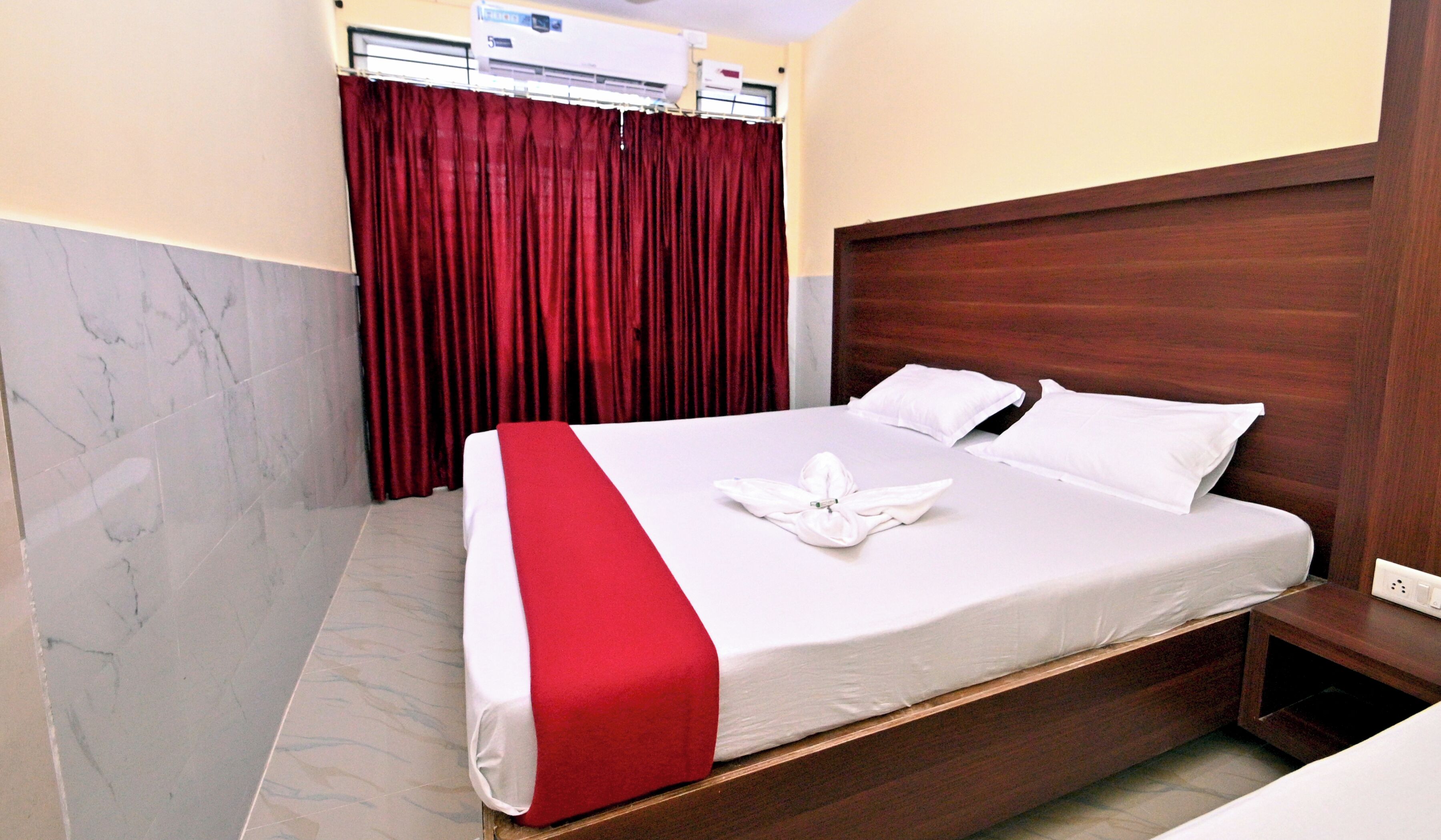 A hotel room with a bed, a wooden headboard, a red curtain, and a marble floor.