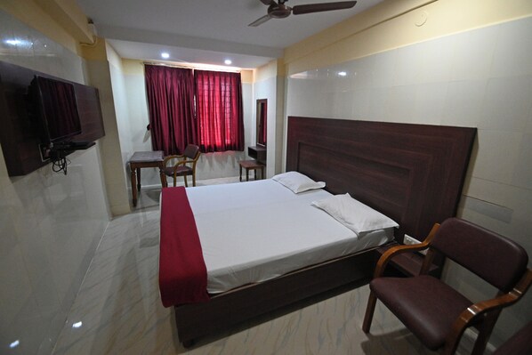Una habitación de hotel con cama, escritorio, silla, televisor y ventilador de techo.